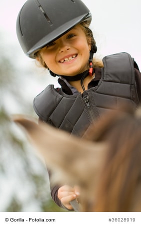Kind reitet mit Weste und Helm auf einem Pferd 